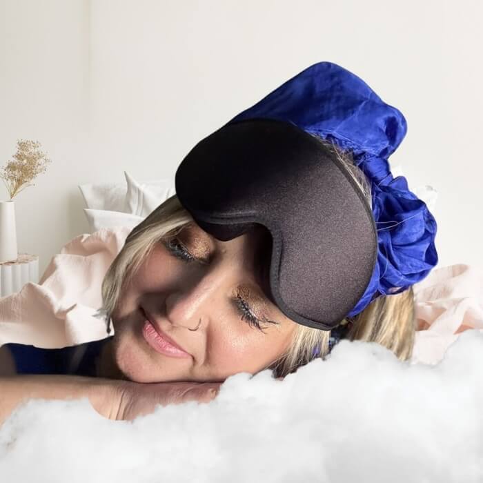 Woman wearing a blue sleep mask and gray pillow on a white background
