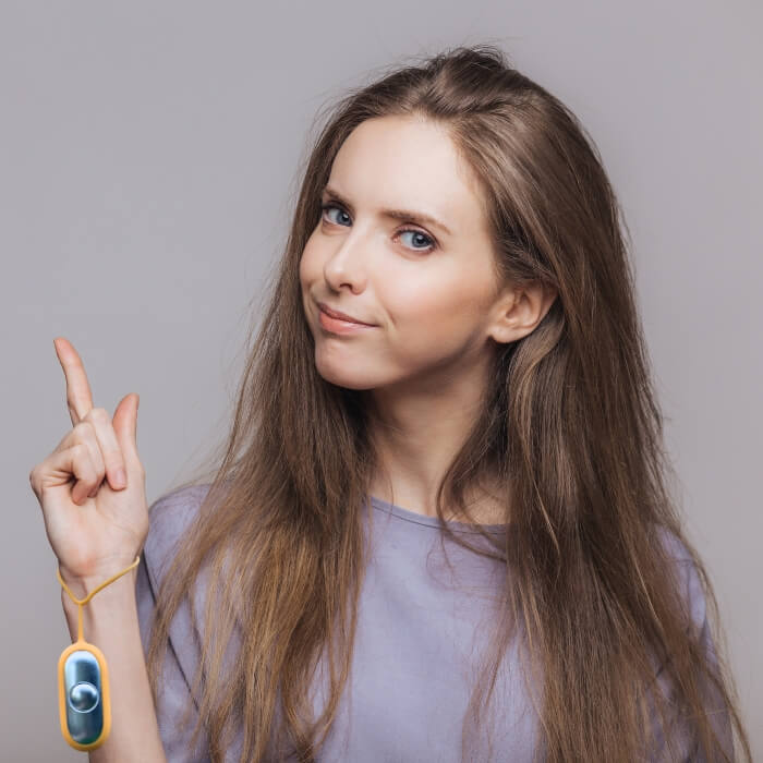 Woman pointing upwards with a neutral expression on a gray background wearing a GoCalm device